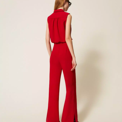 Mulher de costas com conjunto vermelho de camisa sem mangas e calças largas em fundo neutro