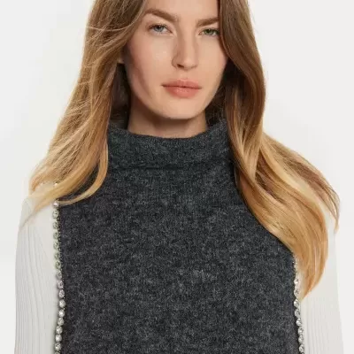 Pessoa com camisola cinza escuro de malha com gola alta e camisa branca com detalhes brilhantes nas laterais