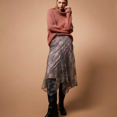 Mulher com camisola rosa, saia cinzenta assimétrica e botas pretas