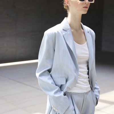 Pessoa em fato azul claro risca de giz e óculos de sol bege grandes.