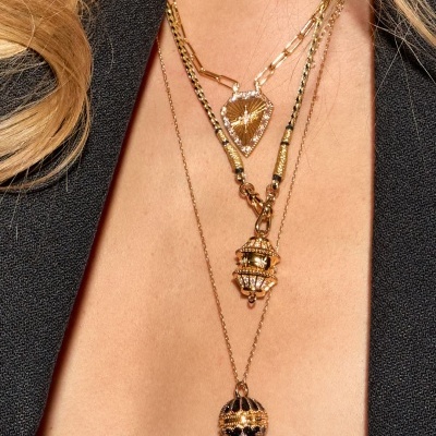 Colares dourados com pendentes variados usados no pescoço de pessoa com casaco preto.