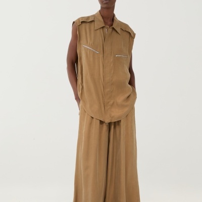 Conjunto feminino bege com camisa sem mangas e calças largas sobre pedras brancas.