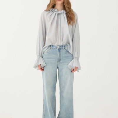 Pessoa com blusa azul clara e calças de ganga largas em chão de pedras claras.