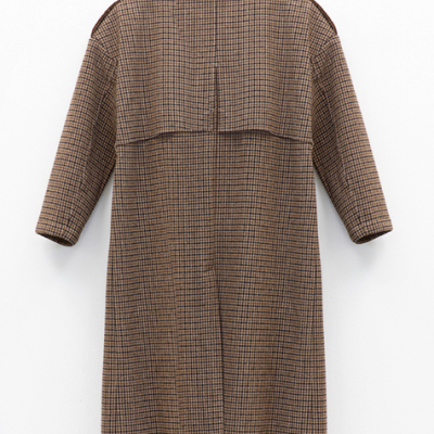 Casaco comprido xadrez castanho e preto pendurado numa parede branca