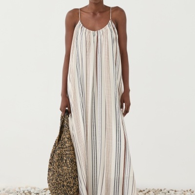 Vestido longo de riscas com sandálias castanhas e bolsa trançada em fundo branco com pedras no chão