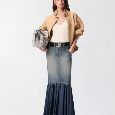 Mulher com casaco camel, top branco, saia jeans comprida, cinto preto e mala animal print.