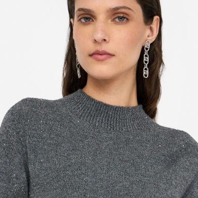 Mulher com sweater cinzento de malha e brincos prateados em fundo branco