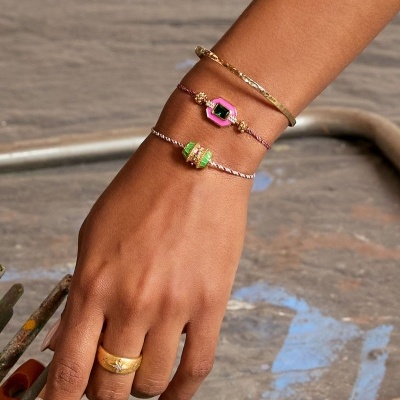 Mão com pulseiras coloridas e anel dourado segurando cabo com etiqueta.