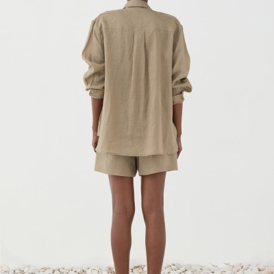 Pessoa de costas com camisa e calções bege e sandálias castanhas em piso de pedras