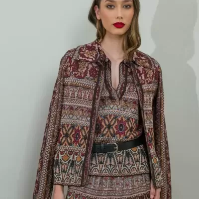 Mulher com vestido e casaco de padrão geométrico colorido, cinto preto e batom vermelho