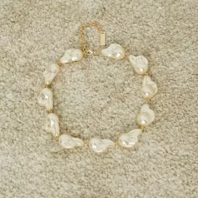 colar de pérolas irregulares creme com fecho dourado sobre tecido bege