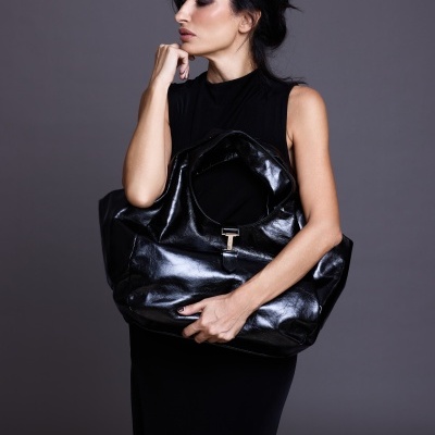 Mala grande preta brilhante com fecho T segurada por mulher em vestido preto