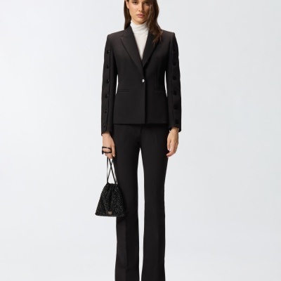 Mulher com conjunto formal preto e camisa branca segurando bolsa preta