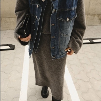 Pessoa com vestido cinzento de malha, colete de ganga azul, botins pretos e bolsa preta
