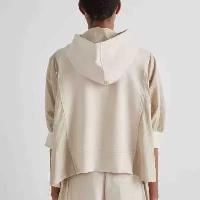 Pessoa vista de costas com colete bege claro e capuz e roupas claras