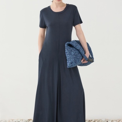 Mulher com vestido longo azul escuro e carteira azul em chão de pedras