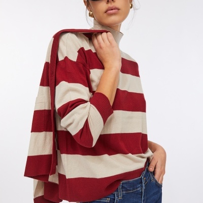 Mulher a usar sweater de malha às riscas bordeaux e bege e jeans azuis com óculos de sol pretos.
