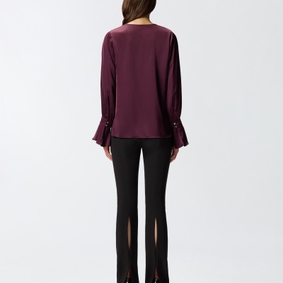 Mulher de costas com blusa vinho acetinada e calças pretas com fendas