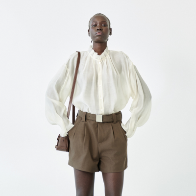 Modelo a usar camisa branca transparente e calções castanhos com bolsa castanha.