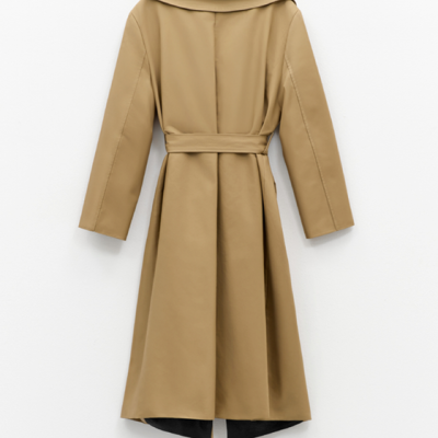 Casaco comprido bege com cinto e gola preta pendurado na parede