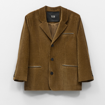 Casaco masculino castanho em veludo cotelê com botões e bolsos frontais, pendurado numa parede branca.