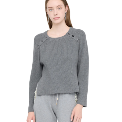 Mulher a usar camisola cinzenta de malha com botões nos ombros e calças cinzentas com detalhes de pérolas