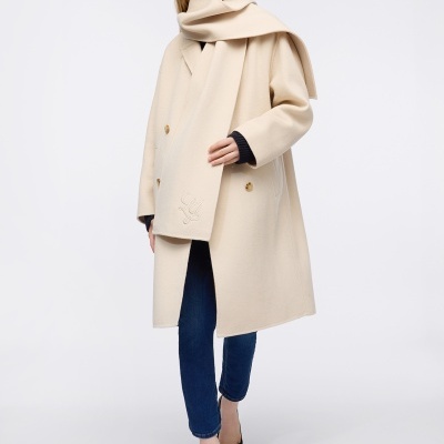 Mulher com casaco creme, cachecol, jeans azul, sapatos pretos e óculos escuros numa pose de moda