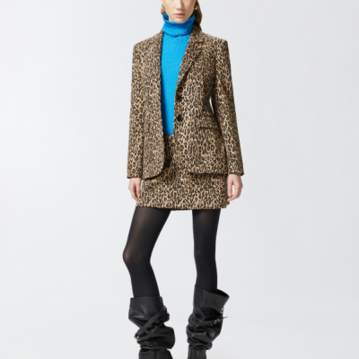 Mulher com roupa padrão animal print, camisola azul e botas pretas num fundo branco