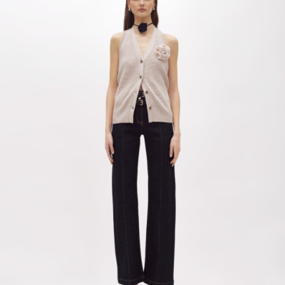 Mulher a usar colete bege de malha com calças pretas largas e sapatos brancos