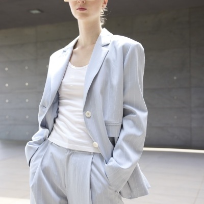 Mulher com blazer e calças riscas azuis claras e t-shirt branca, com óculos de sol creme, em ambiente urbano moderno