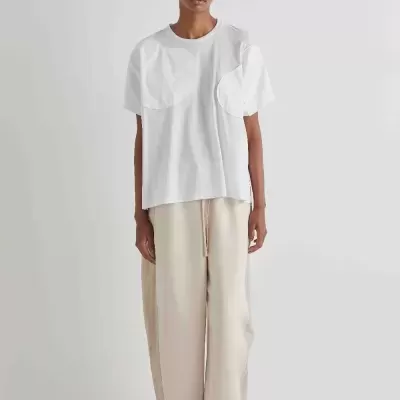 Pessoa com t-shirt branca e calças largas bege em fundo branco