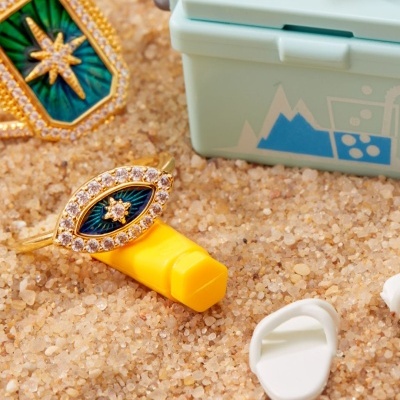 Anéis dourados com pedras e caixa azul clara sobre areia