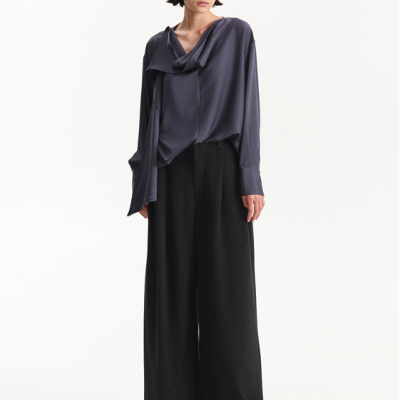 Mulher com blusa azul-escura, calças largas pretas e óculos escuros em fundo branco