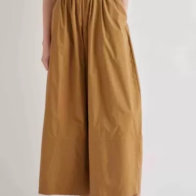 Calças largas castanhas com cintura alta e fivelas, top branco e sapatos baixos brancos