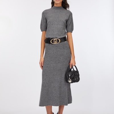 modelo veste camisola cinzenta e saia midi cinzenta com cinto preto e fivela dourada, segura mala preta pequena e usa sapatos pretos de salto