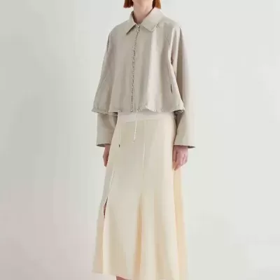 Mulher com casaco bege, saia creme e óculos escuros em fundo branco