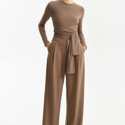 Mulher com conjunto castanho, calças largas, suéter de manga comprida com cinto, botas pretas e óculos escuros grandes