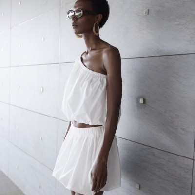 Conjunto branco de top e saia com elástico, em tecido leve, usado numa parede de azulejos cinzentos.