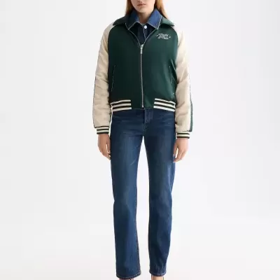 Mulher vestindo casaco bombazina verde escuro com mangas creme e jeans azuis