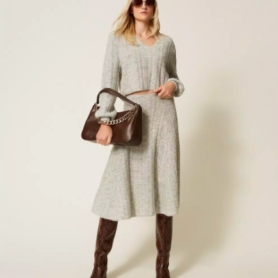 Mulher com vestido cinzento de malha, botas castanhas, óculos escuros e bolsa castanha com corrente dourada