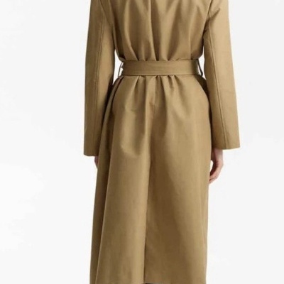 Casaco comprido bege com cinto e gola preta usado por pessoa vista de costas