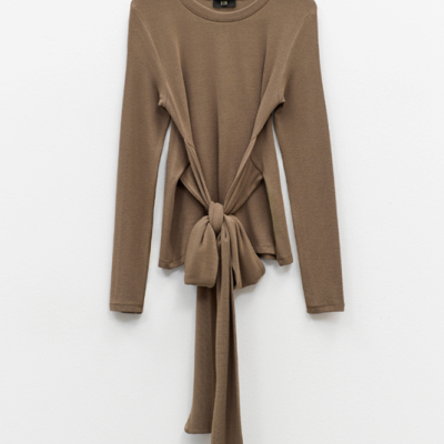 Camisola castanha de malha com mangas compridas e laço frontal pendurada numa parede branca