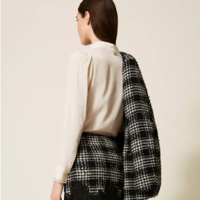 Mulher de costas com camisa creme, saia xadrez preta e branca com renda e casaco xadrez no ombro