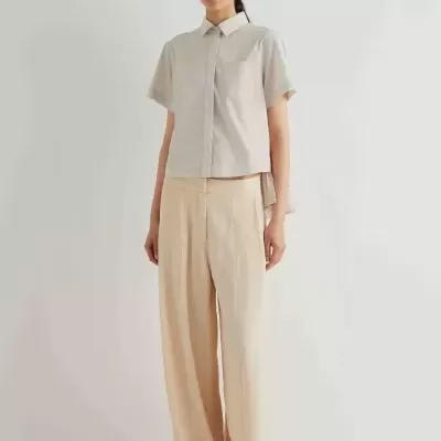 Pessoa de pé a usar camisa bege clara e calças largas bege claro em fundo branco