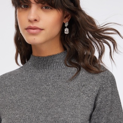 Mulher com camisola cinzenta de malha com gola subida e brincos pendentes com pedras transparentes