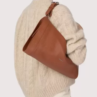 Mala de ombro castanha em pele com alça ajustável usada por mulher de camisola bege