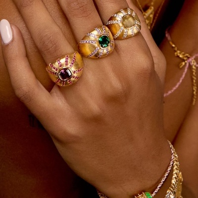 Mão feminina com anéis dourados largos e pulseiras coloridas