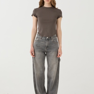 Mulher com t-shirt cinzenta e jeans largos cinzentos e ténis brancos em piso de pedras.