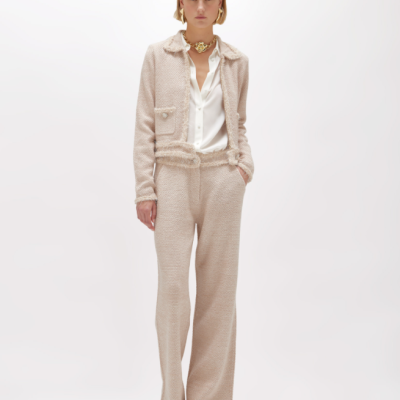 Mulher vestindo conjunto bege texturizado com casaco e calças, camisa branca, sapatos bege e acessórios dourados