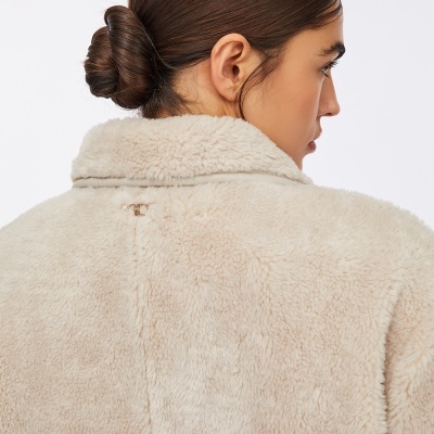 Casaco feminino bege de pelo sintético com gola virada e logo metálico nas costas